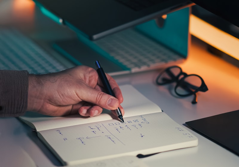 A hand writing notes in a notebook at a desk